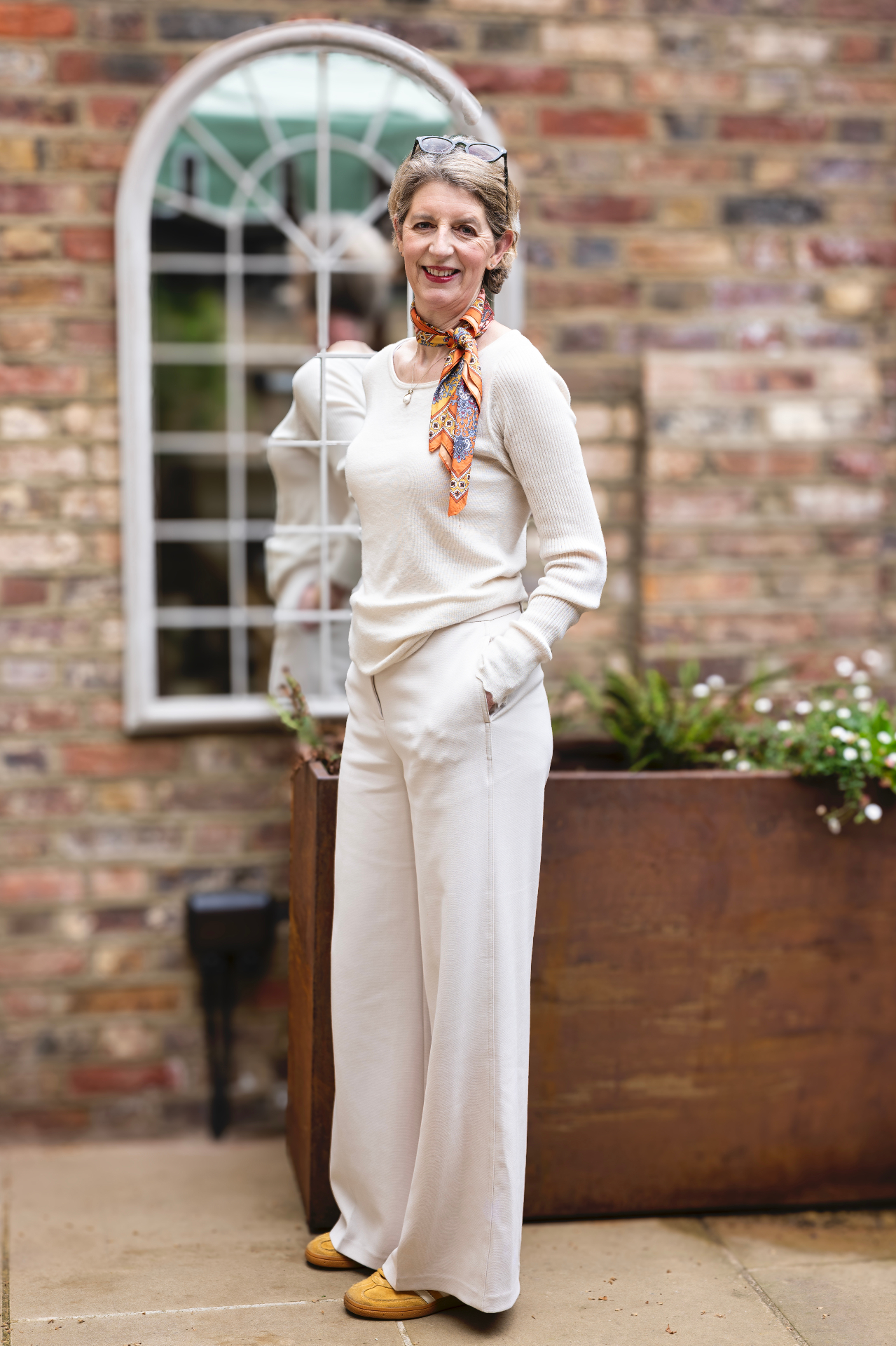 Full-length portrait of Louise Ballard in cream outfit against a brick wall