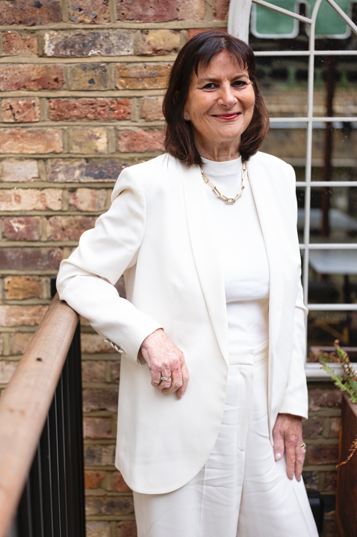 Full-length portrait of Victoria Tomlinson in a cream suit beside a brick wall