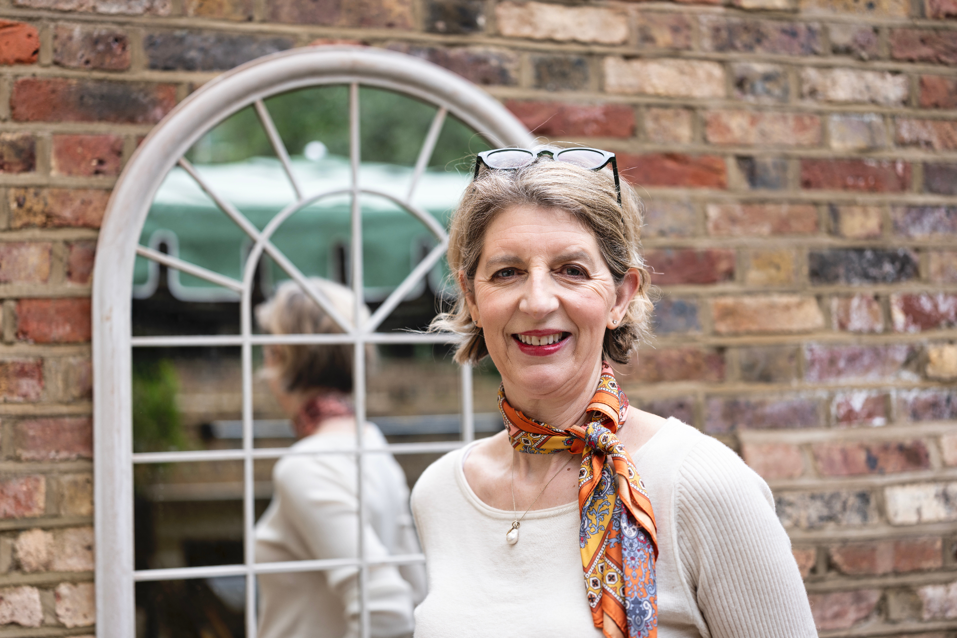 Portrait of Louise Ballard smiling in front of a brick wall with arched window